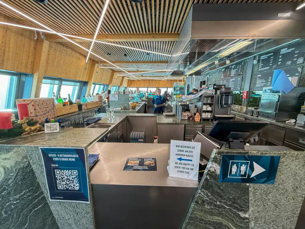view of the restaurant inside the Matterhorn Glacier Paradise, with informational signs displayed and a kitchen in the background