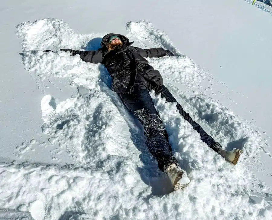 girl in black ski jacket and pants making a snow angel at the top of Matterhorn Glacier Paradise