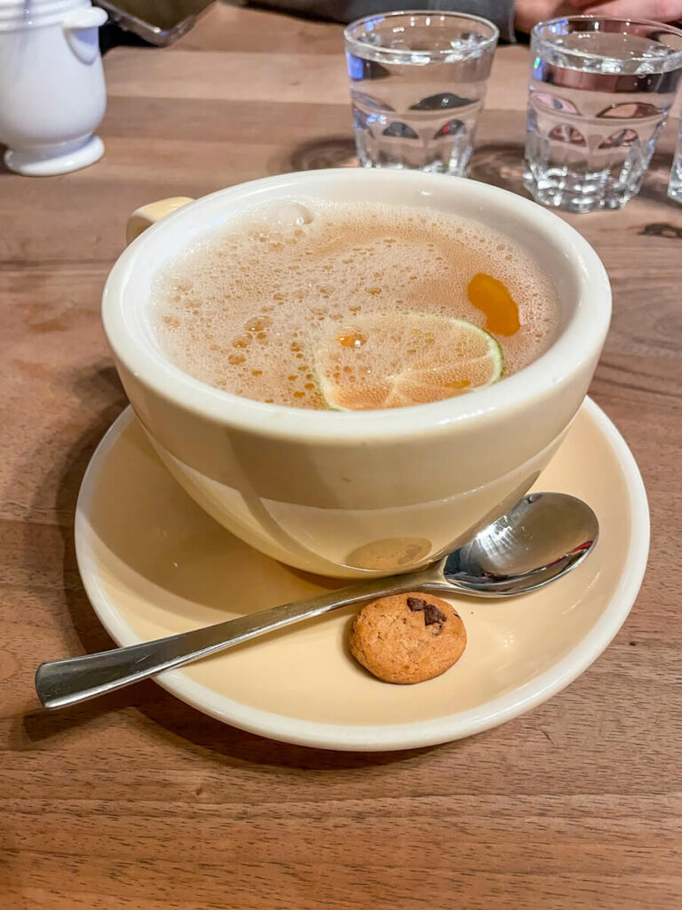 Cup of hot tea with a lemon slice and a mini chocolate chip cookie on a wooden table at MANUD in Zermatt